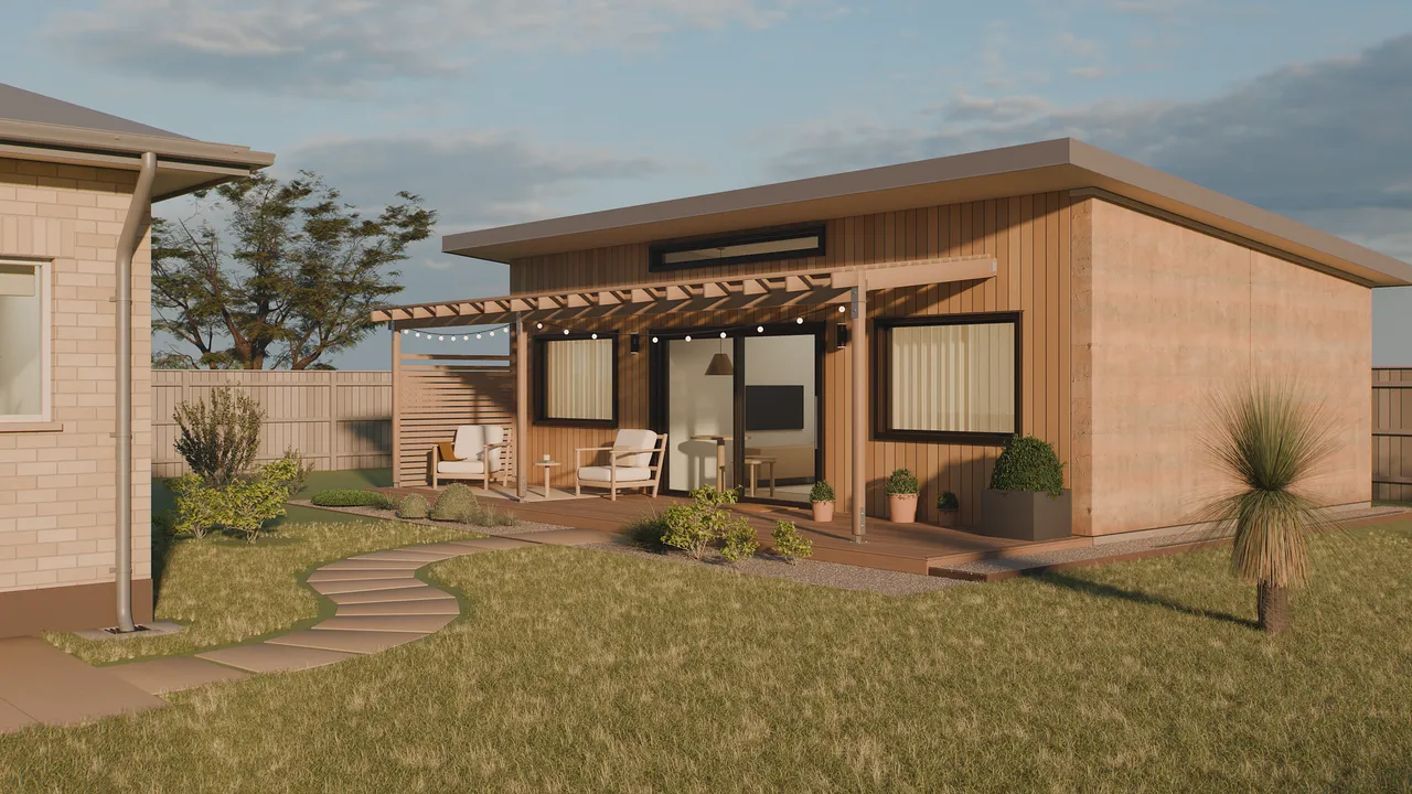 Seed 60, a 60 square metre backyard home with timber cladding, a rammed earth wall and a covered deck, behind a brick house in Adelaide at golden hour.